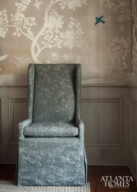 Wingback chair upholstered in blue patterned fabric against a wall with a chinoiserie-style wallpaper featuring trees and birds.