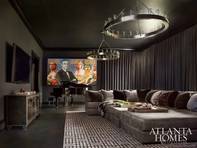 Dark gray room with a large sectional sofa, a grand piano, a James Bond movie poster, and two circular chandeliers.
