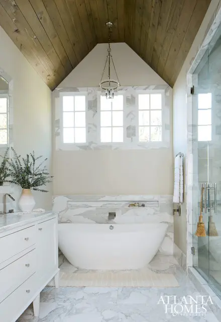 Modern bathroom with a freestanding white tub, marble tile accents, a wood plank vaulted ceiling, and a glass-enclosed shower.