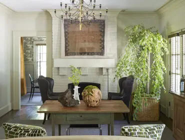 Living room with white brick fireplace, large tapestry, dark leather wingback chairs, and a rustic wooden table with decorative objects.