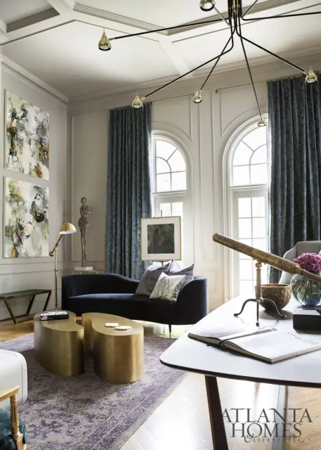 Living room with navy chaise sofa, abstract art, brass sculptural coffee tables, and a vintage telescope on a desk.