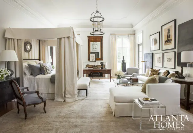 Spacious bedroom with a four-poster bed, sitting area with white sectional sofa, and a desk in front of a fireplace.