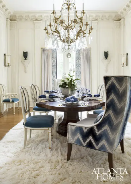 Formal dining room with a dark wood table set for a meal, blue velvet chairs, a crystal chandelier, and a plush cream rug.