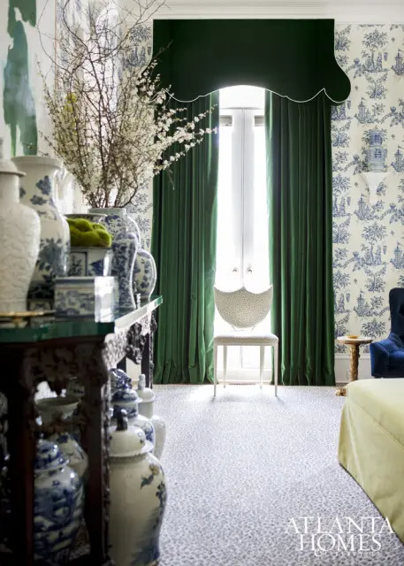 Elegant living room with blue and white Chinoiserie wallpaper, deep green velvet curtains, and a collection of blue and white porcelain vases on a dark wood console table.