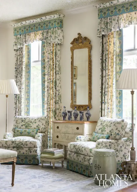 Living room with floral upholstered armchairs, ornate gold mirror, blue and white vases on a dresser, and patterned curtains.