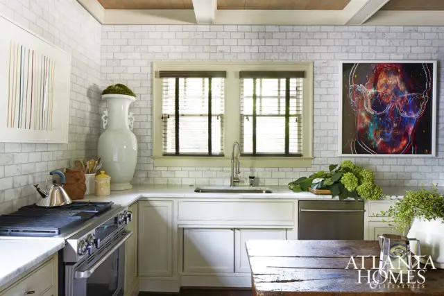 White subway tile kitchen with a stainless steel range, marble countertops, a farmhouse sink, and a colorful abstract portrait above the sink.