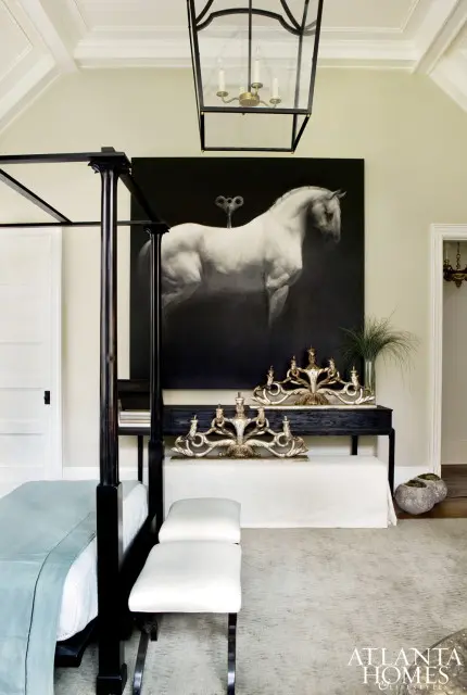 Bedroom with a dark wood four-poster bed, white upholstered bench, and a large black canvas painting of a white horse with a wind-up key