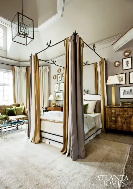 Bedroom with a four-poster bed draped in taupe and gold fabric, a vintage dresser, and a sofa with green pillows.