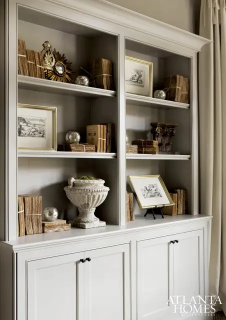 Built-in gray shelving unit filled with stacks of old books, framed artwork, decorative spheres, and a stone urn.