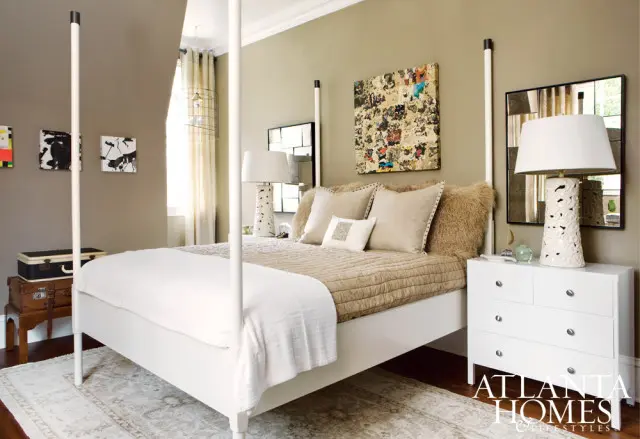 Bedroom with a white four-poster bed, taupe walls, a textured quilt, and decorative pillows. Artwork hangs on the wall above the bed.
