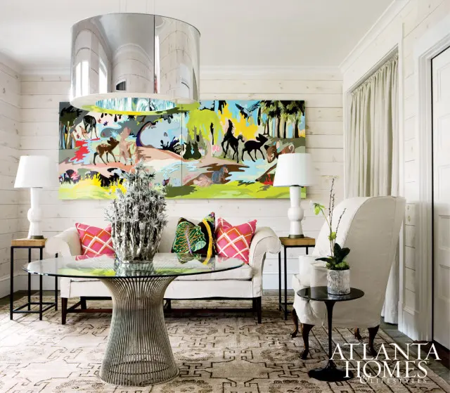 Living room with white shiplap walls, a white sofa, and a large colorful abstract painting of animals. A chrome table with a glass top sits in front of the sofa.
