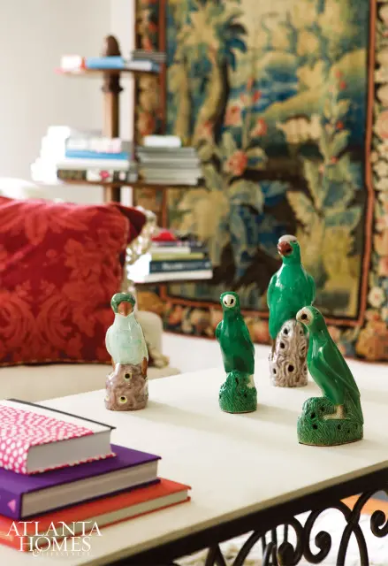 Living room with a tapestry wall hanging, a red patterned throw pillow, and a coffee table displaying ceramic bird figurines and stacked books.