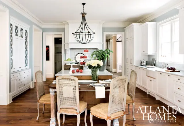 Light blue walls and white cabinetry in a kitchen with a large island, cane-backed chairs, and a wrought iron chandelier.