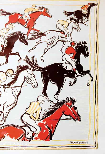 Illustration of a horse race with jockeys on horseback in red, black, and white, with a light blue background and a thin yellow border.