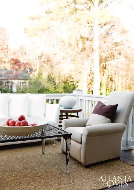 Outdoor seating area with a white sofa, a beige armchair with a maroon and beige pillow, and a metal coffee table holding a bowl of red apples.