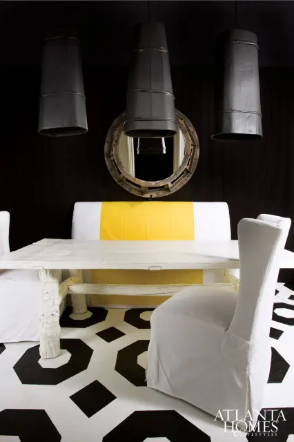 Dining room with a white rustic table, white slipcovered chairs, black and white geometric floor, and three dark barrel pendant lights above a round wooden mirror.