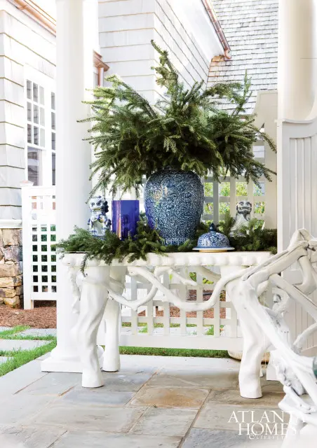 White console table with a large blue and white ginger jar filled with evergreen branches, foo dog figurines, and a blue vase.