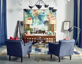Living room with two navy blue armchairs facing a wooden desk with a colorful abstract painting above it. Blue curtains frame the scene.