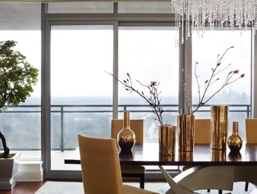 Dining room with dark wood table, gold vases with branches, and orange upholstered chairs, overlooking a city skyline through floor-to-ceiling windows.