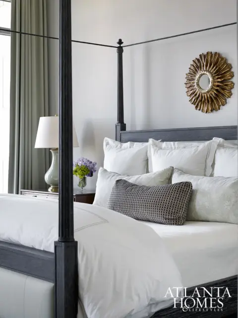 Bedroom with a dark wood four-poster bed, white bedding, a patterned lumbar pillow, and a sunburst mirror on the wall.