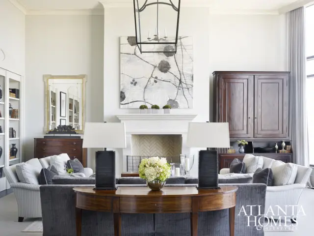 Living room with a fireplace, flanked by two sofas and a dark wood cabinet. A large abstract painting hangs above the fireplace.