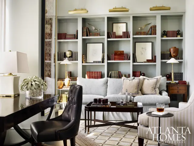 Light blue built-in bookshelves filled with books and decorative objects, flanking a light gray sofa with patterned throw pillows. A dark wood desk and chair are in the foreground.