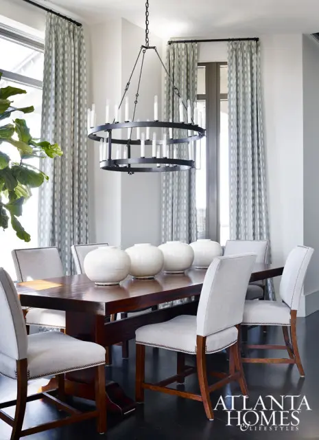Dining room with dark wood table, upholstered chairs, patterned curtains, and a circular chandelier.