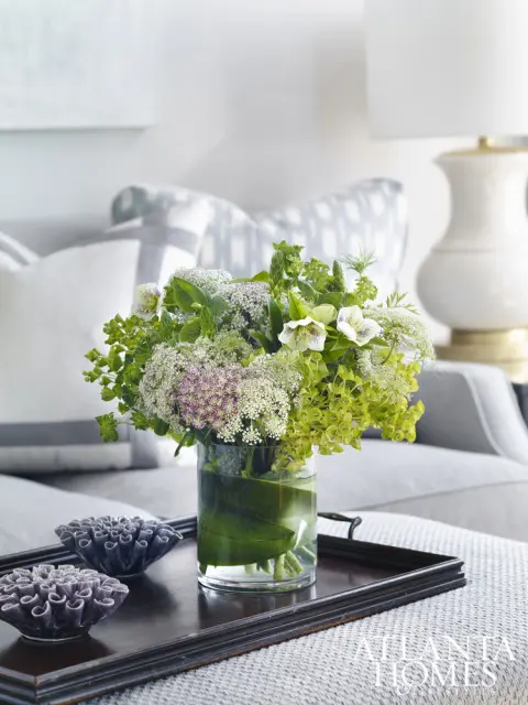 Living room vignette with a floral arrangement in a glass vase on a dark wood tray, next to decorative coral-like objects.