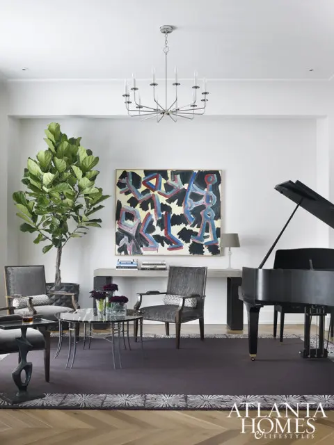 Living room with a grand piano, abstract art, a fiddle leaf fig tree, and upholstered chairs around a glass-top coffee table.