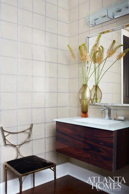 Powder room with textured wallpaper, a floating dark wood vanity with a glass countertop, a modern faucet, and a decorative metal chair with a dark seat.