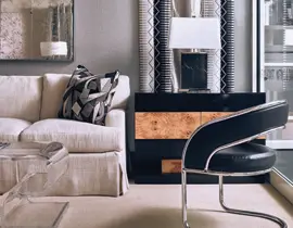 Cream slipcovered sofa with geometric pillows next to a black lacquered cabinet with burl wood accents and a chrome chair with black leather seat.