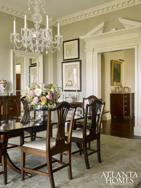 Formal dining room with dark wood table and chairs, crystal chandelier, floral centerpiece, and framed maps on the wall.