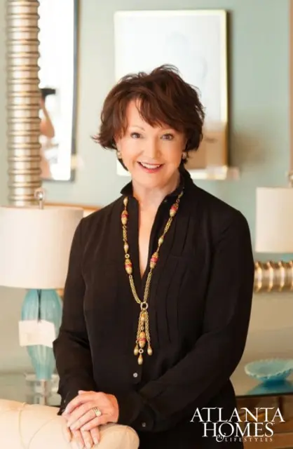 Woman with short brown hair wearing a black blouse and a long gold necklace with pink and gold beads. She is smiling and wearing rings on her left hand. The Atlanta Homes & Lifestyles logo is in the lower right corner.