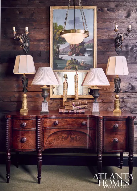 Mahogany sideboard with carved details topped with four lamps, books, and a landscape painting above a mirror.
