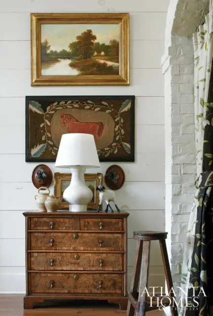 Wooden dresser with antique artwork and decorative objects, including a white lamp, a sheep figurine, and two small portraits.