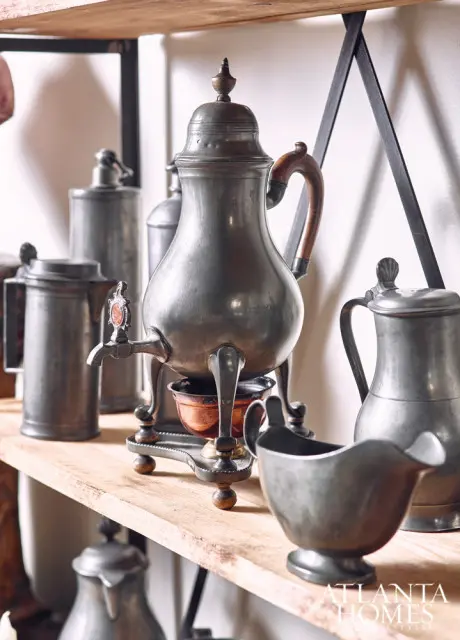 Collection of antique pewter serving vessels including a large urn with a spigot, a pitcher, and a gravy boat, displayed on a wooden shelf.