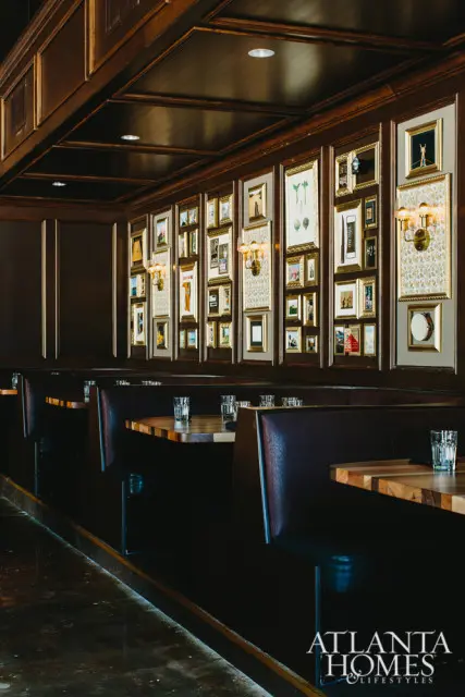 Dark wood paneled dining room with leather booths, wooden tables, and a wall of framed art and sconces.