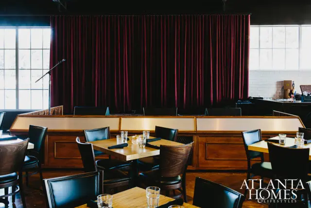 Dining room with dark wood tables and chairs, a burgundy velvet stage curtain, and large windows.
