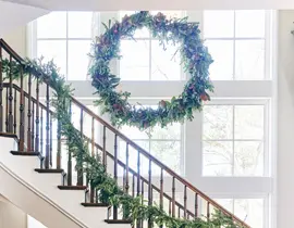Wooden staircase with garland draped along the banister, topped by a large circular wreath hanging from the upper window frame.