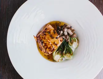 Seared salmon fillet with a glaze, served with baby bok choy and mushrooms on a white plate.