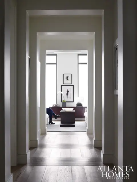 Hallway with light wood floors and white trim leading to a living area with a dark wood console, coffee table, and artwork on the wall.