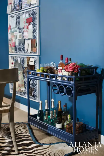 Blue bar cart with bottles of champagne, liquor, and glasses, next to a chair with a zebra print rug.