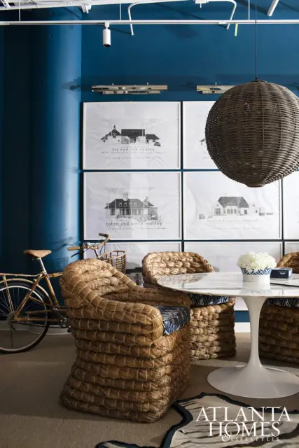Woven rattan chairs surround a marble-top tulip table against a teal wall displaying framed architectural drawings. A vintage bicycle with a basket is parked nearby.