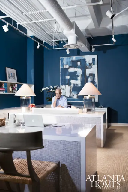 Office with deep blue walls, white desks, and a man sitting at one desk. A large abstract painting hangs on the wall.