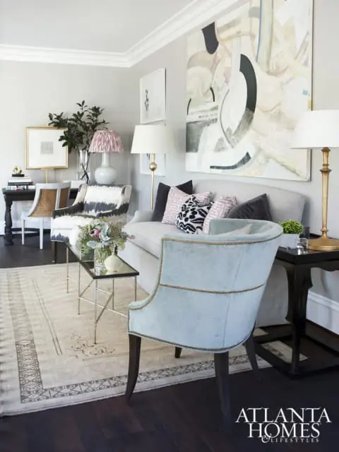 Light gray living room with a light gray sofa, abstract art, patterned accent chairs, a patterned rug, and a light blue upholstered chair with nailhead trim.