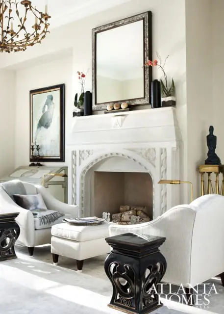 Living room with a white stone fireplace, ornate mirror, artwork, and upholstered furniture.