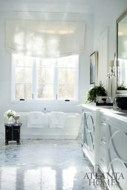 White bathroom with freestanding tub, patterned floor tiles, and white double vanity with marble countertop.