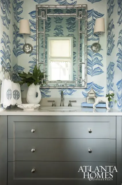 Powder room with blue and white palm leaf wallpaper, a silver bamboo-style mirror, and a gray vanity with a white countertop and silver hardware.