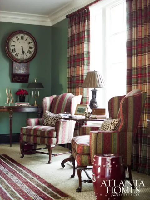 Green room with plaid curtains, striped armchairs, a large wall clock, and a red ceramic garden stool with the Atlanta Homes & Lifestyles logo.