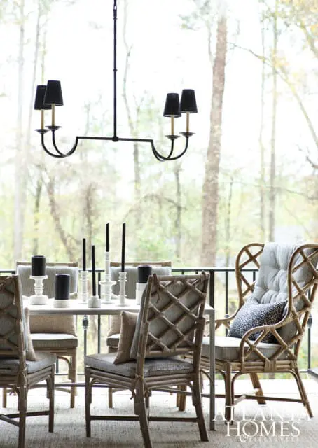Dining set on a screened porch with wicker chairs, striped cushions, and a black chandelier. A table is set with white candlesticks and black candles.